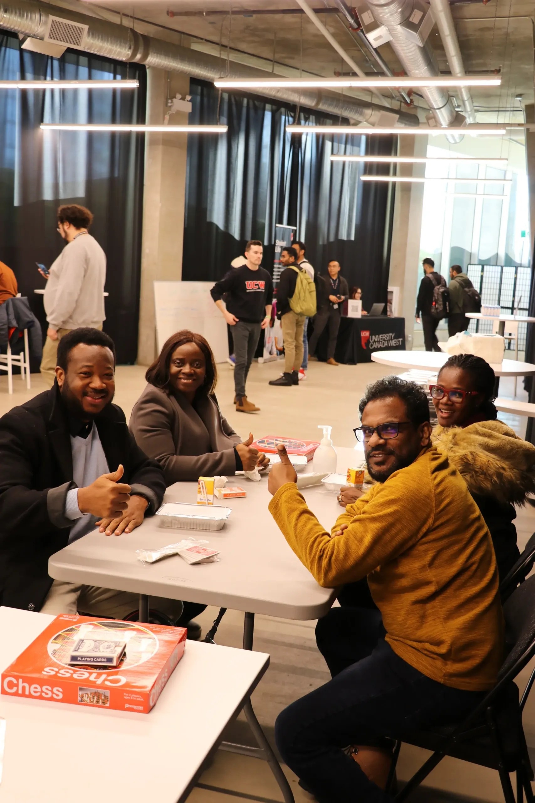 4 smiling students are playing board games in a common area.